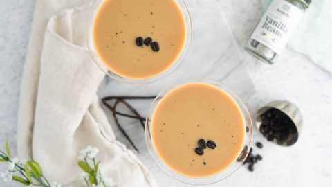 Vanilla espresso martini in martini glass with vanilla beans and marble background