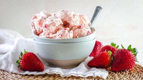 Stawberry ice cream in a bowl with strawberries on a table