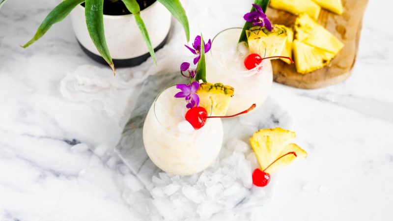 Two Pina Colada cocktails with tropical fruit, cherries and ice