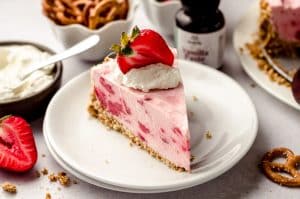 Creamy Strawberry Pie with crumbly crust topped with strawberry and whipped cream on a white plate