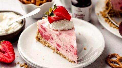 Creamy Strawberry Pie with crumbly crust topped with strawberry and whipped cream on a white plate