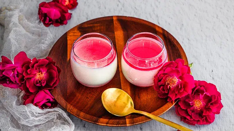 Vanilla Milk Pudding with bright pink hibiscus syrup in cups on a wooden serving plate with flowers scattered about