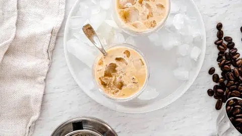 Vietnamese vanilla coffee with creamer, on a cutting board with neutral background and coffee beans