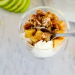 Apple pie in a jar with whipped cream on a neutral background with apple slices