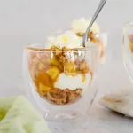 Apple pie in a jar with whipped cream on a neutral background with apple slices