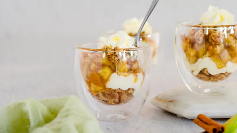 Apple pie in a jar with whipped cream on a neutral background with apple slices