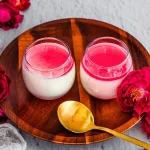 Vanilla Milk Pudding with bright pink hibiscus syrup in cups on a wooden serving plate with flowers scattered about