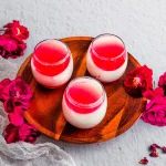 Vanilla Milk Pudding with bright pink hibiscus syrup in cups on a wooden serving plate with flowers scattered about