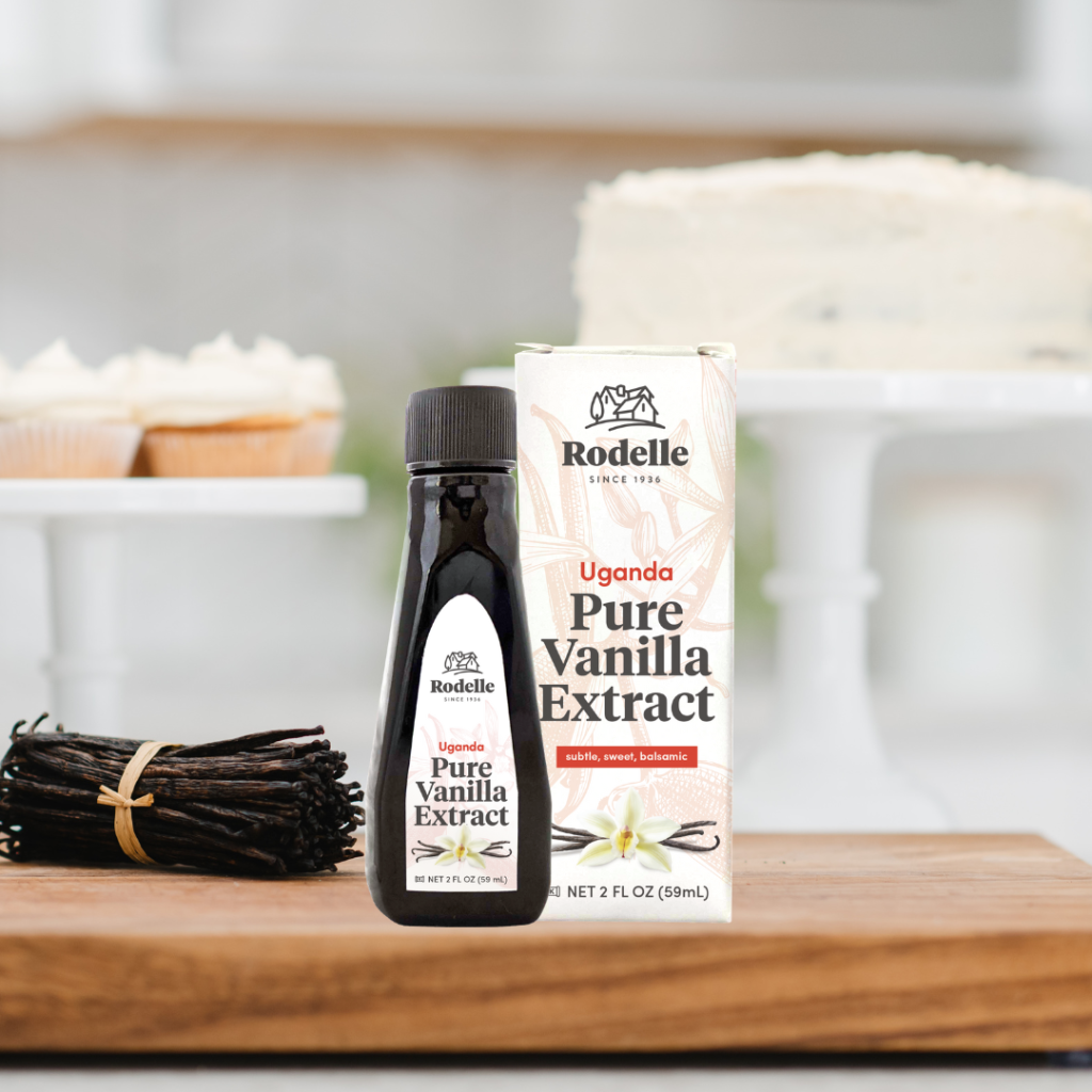 Ugandan Vanilla in a bottle with a box on a cutting board with cupcakes and vanilla beans