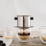 Vietnamese vanilla coffee with creamer, on a cutting board with neutral background and coffee beans