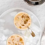 Vietnamese vanilla coffee with creamer, on a cutting board with neutral background and coffee beans