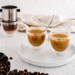 Vietnamese vanilla coffee with creamer, on a cutting board with neutral background and coffee beans