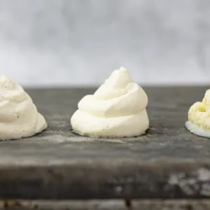 Close up of piped whipped cream made with powdered sugar laying on a meta textured tray.