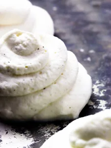 close up of piped whipped cream with vanilla flecks laying on top of a gray textured pan