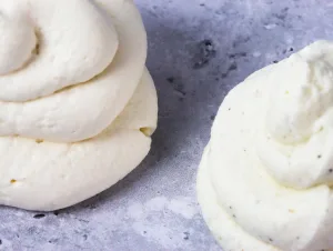 close up of two piped whipped cream dallops. The left is made with granulated sugar while the right is made with vanilla paste so you can see flecks of vanilla.