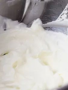 Close up of beaten whipped cream made with granulated sugar in a metal bowl.