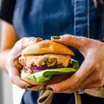 A person holding a turkey burger in their hand. Their clothing is blue jean material, nails were paainted green