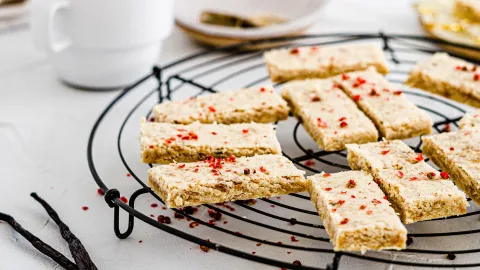 Pink Peppercorn Top angle shot of pink peppercorn shortbread slices laying on a black wire cooling rack. Surrounding the cookies are vanilla beans, and a white mug.