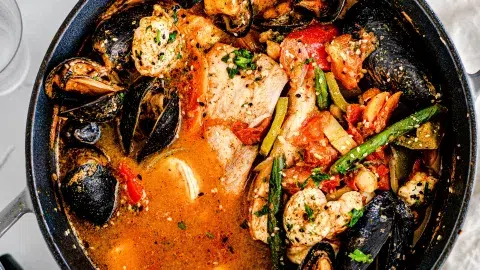 Top close up shot of seafood tagine including white fix, mussels, jumbo shrimp, potatoes, and many veggies in a warm broth.