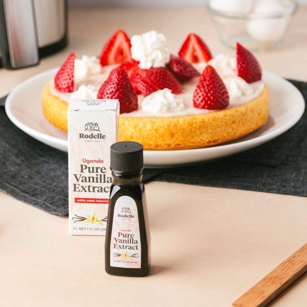recipe image of a vanilla airfryer cake with dollops of whipped cream and strawaberries on top. In the background of the cake is white tile and an airfryer. in the front is Rodelle 1oz uganda pure vanilla extract