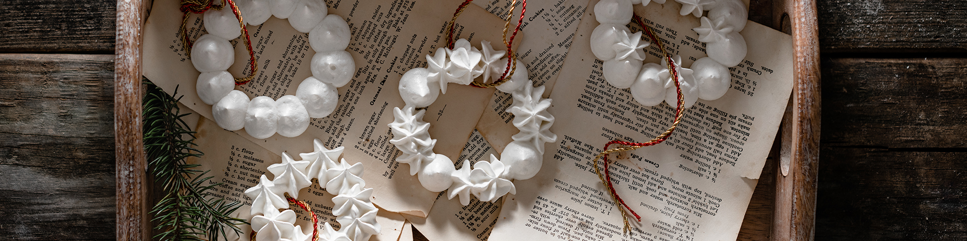 Meringue Christmas Wreath Ornaments shown on old recipe paper in wooden serving tray on wood background from overhead angle with ties for decorating