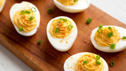 Above angle shot of homemade sriracha deviled eggs. Six deviled eggs lay on a skinny wooden board and are garnished with Rodelle sriracha seasoning and green onions.
