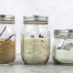 Side profile view of three mason jars with different types of vanilla bean sugar. The left mason jar is cane sugar, the middle is monk fruit, and the right is regular granulated sugar.