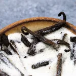 Close up of vanilla bean sugar and chopped vanilla beans in the sugar. The sugar is set in an earth toned flat bowl and