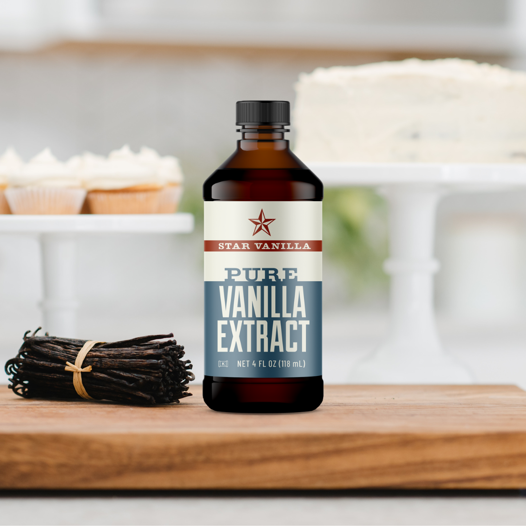 bottle of star vanilla extract on cutting board with vanilla beans and cakes and cupcakes in background
