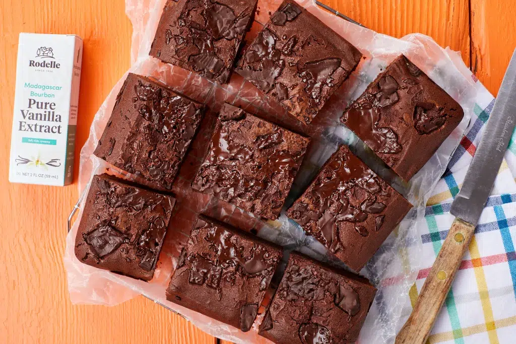 9 brownies on orange background and a piece of parchment paper with a bottle of vanilla extract