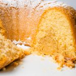Side close up photo of the kentucky butter bundt cake showing the inside of the cake. You can see the central part of the bundt cake has more sugar and butter while the outer layer is light and fluffy. the cake stands on a white cake stand and the background is a glass vial with some dried plant accessory.