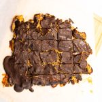 top shot of a whole chocolate with peanut butter covered date bark. The organic block sits on a wooden cutting board with white parchment paper.
