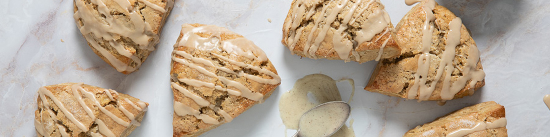 Vietnamese Coffee Scones shown from overhead angle on marble countertop with coffee glaze and a serving spoon with bowl of glaze slightly out of frame