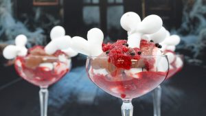 wide shot of an eton a bloody mess. The granita is red along with chocolate chips and white cookie bones. They're served in clear tall wide cocktail glasses.