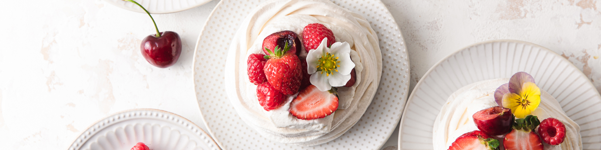 Mini Vanilla Bean Pavlovas with Vanilla Whipped Cream shown on 4 individual plates with berries and edible flowers, shown from an overhead angle