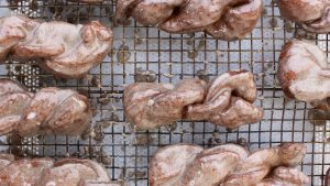 top view of a witches brew twists on a black cooling rack. Below the cooling rack is parchment paper. You can see a delicious vanilla bean glaze on each twist