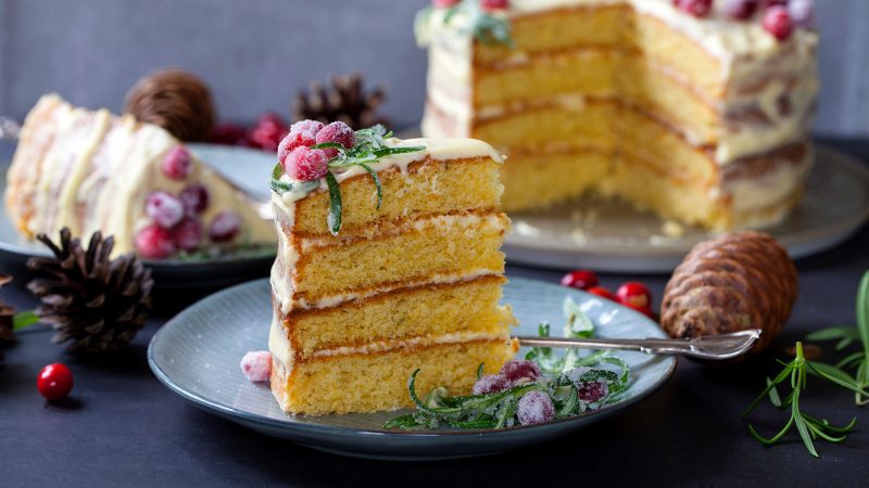 layered cranberry orange cake on grey plate with cake slice and cake in background